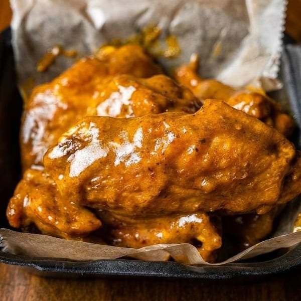 Close-up of several saucy chicken wings in a black container lined with parchment paper.