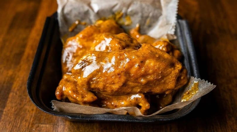 Close-up of several saucy chicken wings in a black container lined with parchment paper.